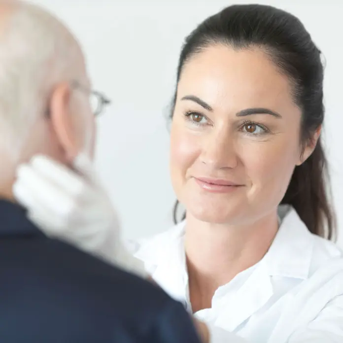 Ärztin untersucht Patienten am Hals