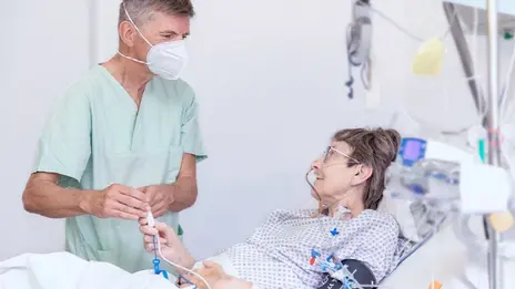 Dr. Dirk Risack, Oberarzt, spricht mit einer Patientin im Bett. Sie ist auf dem Weg der Besserung. 