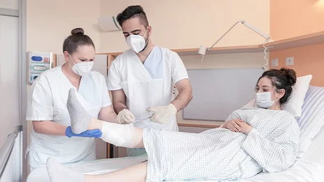 Zwei Mitarbeitende kümmern sich um das Bein einer Patientin. 