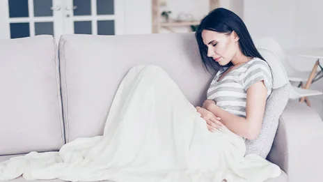 Auf dem Sofa liegende Frau mit Schmerzen im Bauchbereich