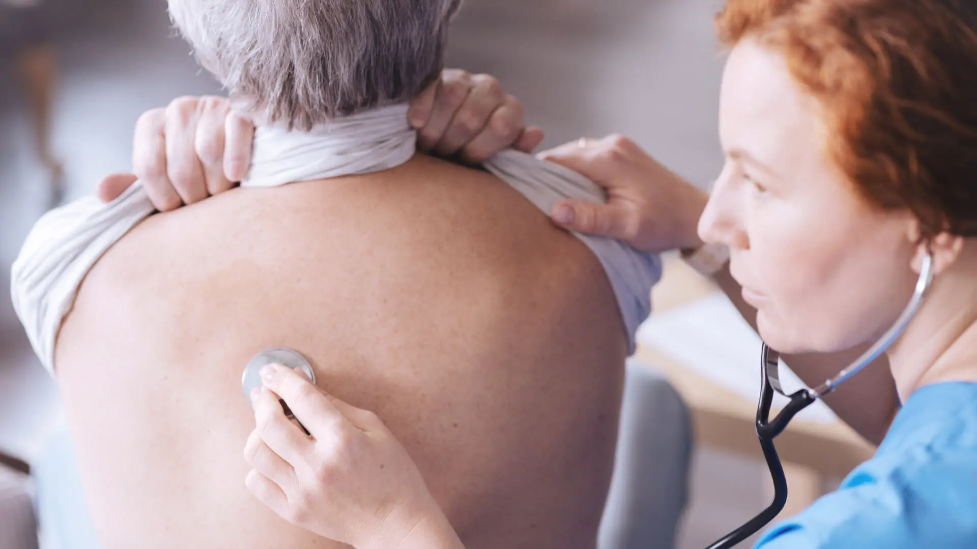 Eine Ärztin horcht mit dem Stethoskop den Rücken eines Patienten ab.